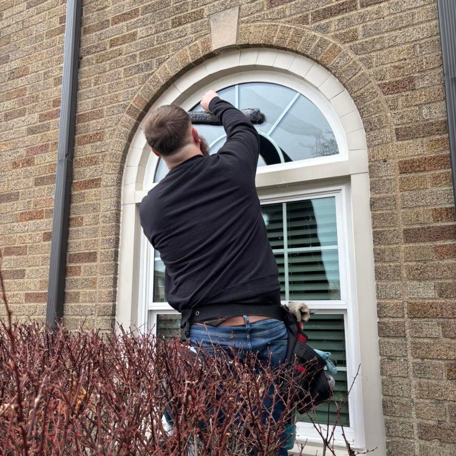Crew member cleaning an arched window from a ladder