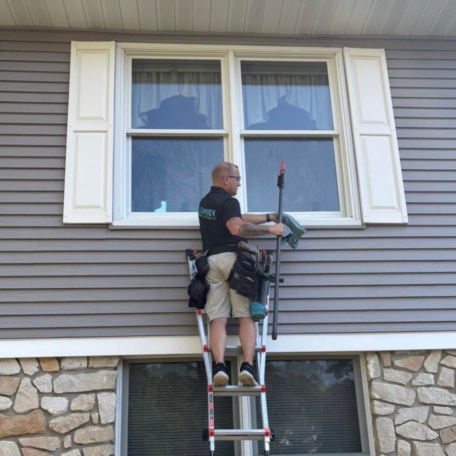 Crew member cleaning a home's windows from a ladder